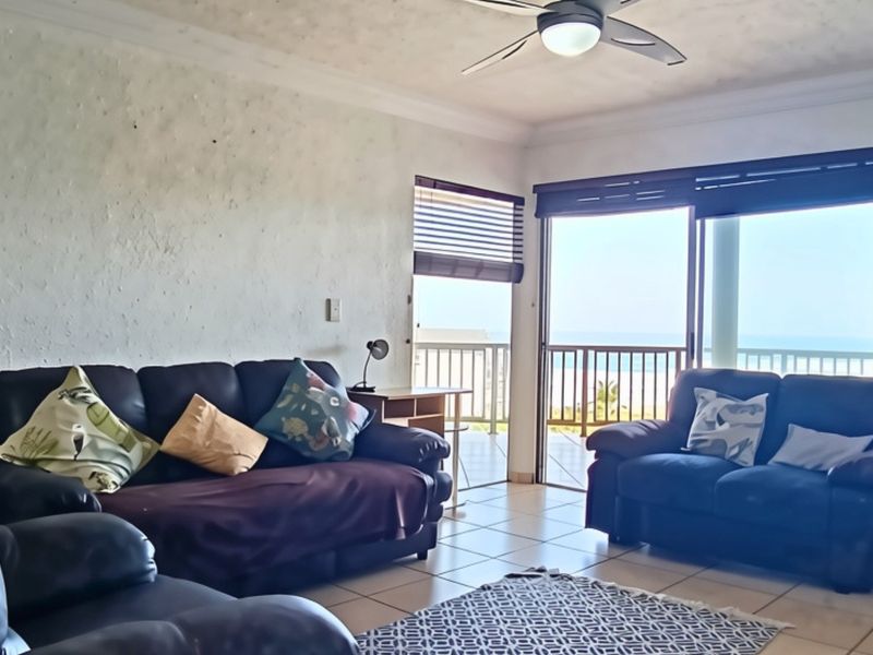 A living room featuring tiled flooring, a ceiling fan, and sliding glass doors that open onto a balcony with ocean views.