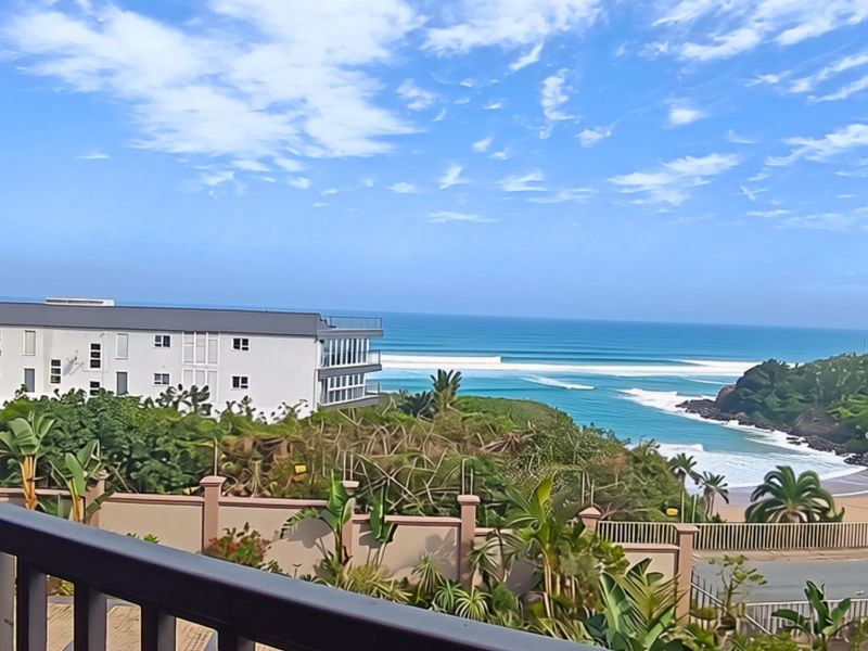A scenic coastal view overlooking the ocean, beach, and surrounding landscape from an elevated balcony perspective.