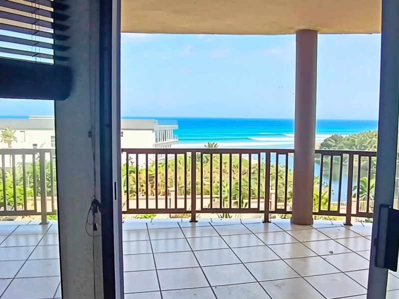A spacious covered balcony featuring tiled flooring and a balustrade, offering expansive ocean and coastal views.
