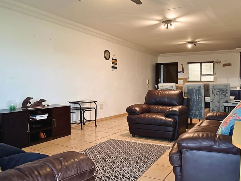 An open-plan living and dining area featuring tiled flooring, ceiling fans, and a connected kitchen space with built-in cabinetry.