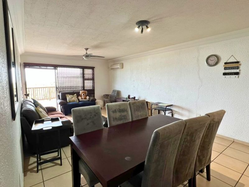 Open-plan living and dining area featuring tiled floors, a ceiling fan, air conditioning, and access to a balcony through sliding glass doors.