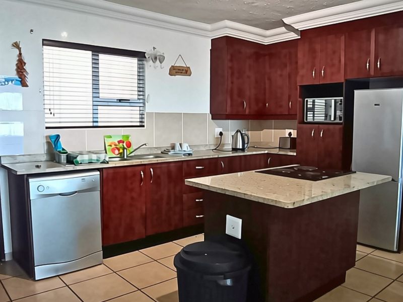 A functional kitchen featuring dark wood cabinetry, granite countertops, a central island with a hob, and tiled flooring.