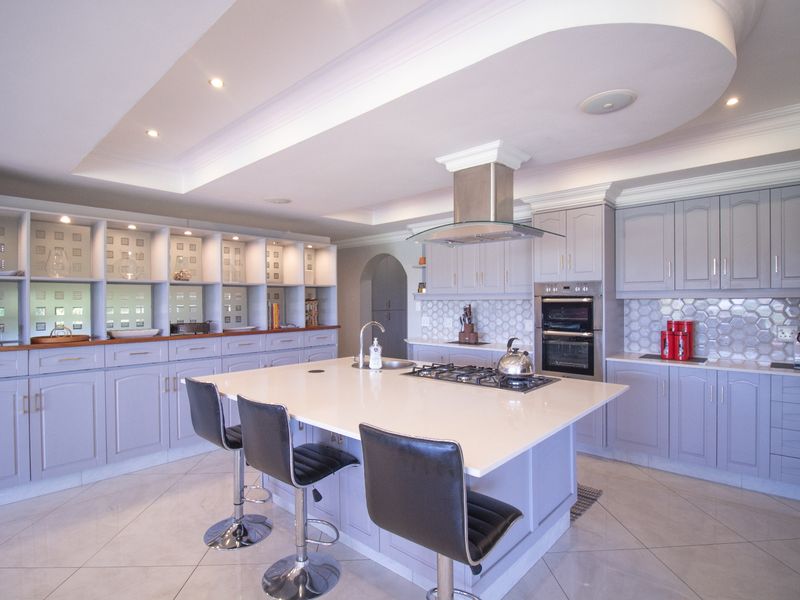 Spacious modern kitchen featuring a large central island, built-in oven, gas hob, extractor fan, and extensive cabinetry with a stylish tiled backsplash.