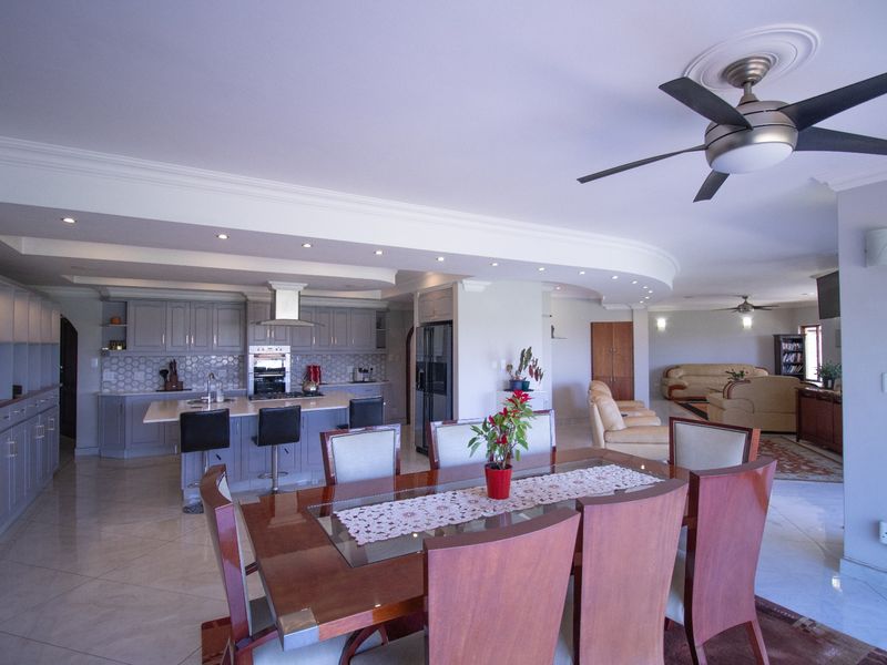 Spacious open-plan living area featuring a modern kitchen with island, built-in cabinetry, and integrated appliances, flowing into a dining and lounge space.