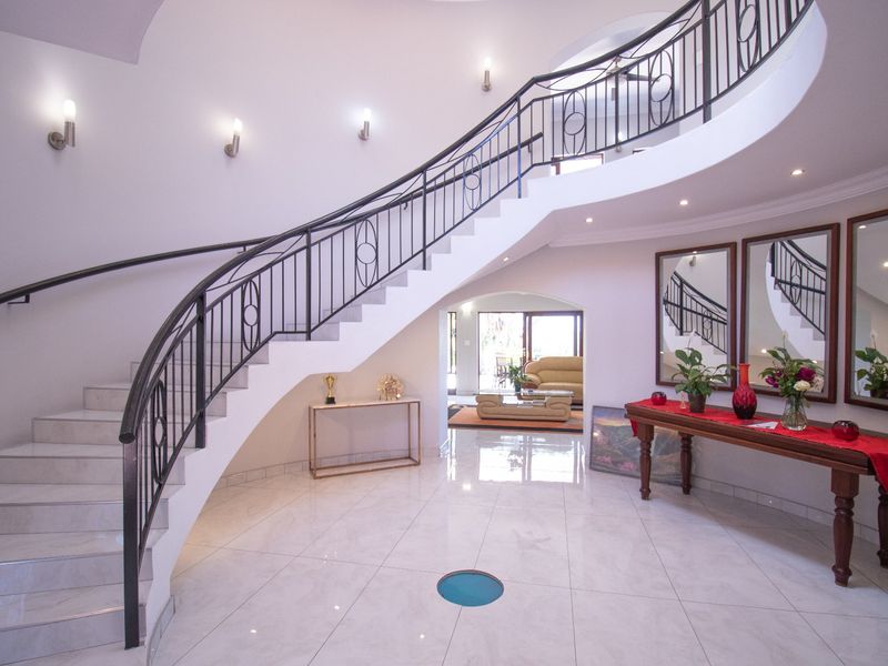 Grand entrance foyer featuring a striking curved staircase with wrought iron balustrade, polished tiled flooring, and elegant wall lighting.