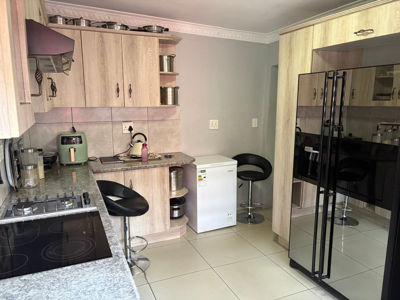 A functional kitchen featuring light wood-look cabinetry, granite countertops, dual hob setup, and tiled flooring with decorative ceiling cornicing.