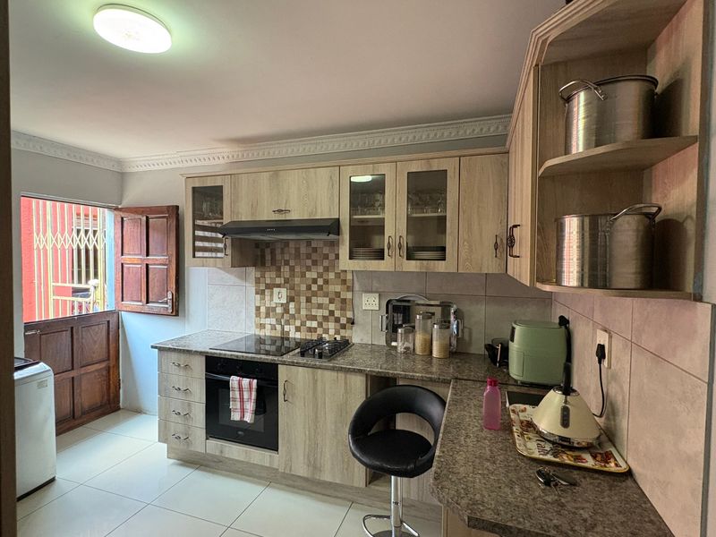A functional kitchen featuring light wood-finish cabinetry, granite-look laminate countertops, a built-in oven and hob, and a tiled backsplash.
