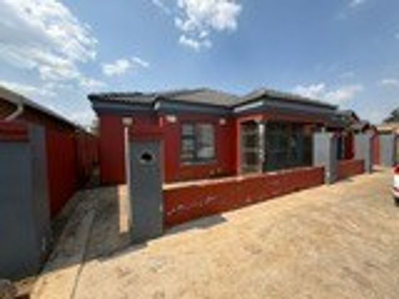 Front exterior view of a single-story house featuring a tiled roof, paved driveway, and a perimeter boundary wall with a security gate.