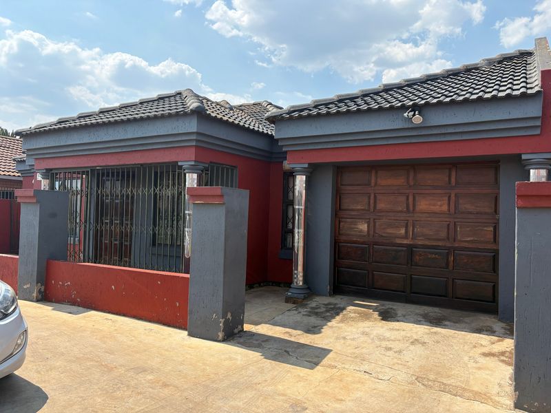 Front elevation of a house featuring a concrete driveway, wooden garage door, and decorative pillars with security bars on the windows.