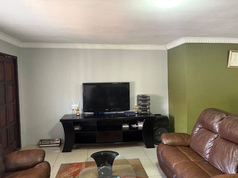 A living room featuring tiled flooring, crown molding, and a neutral color scheme with an accent wall.