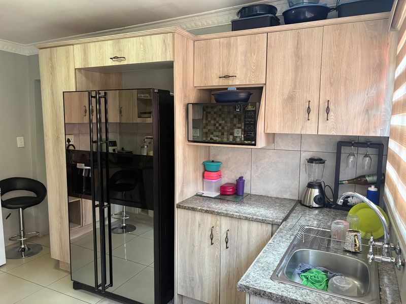 A functional kitchen featuring light wood-look laminate cabinetry, granite countertops, a stainless steel sink, and a built-in microwave with tiled backsplash.