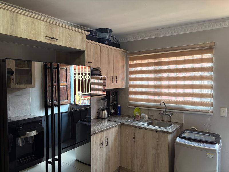 A functional kitchen featuring light wood-grain cabinetry, granite-look countertops, a stainless steel sink, and modern window blinds.