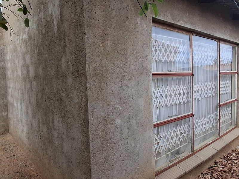 A view of the rear exterior elevation featuring a concrete rendered wall, corrugated metal roofing, and metal security window grilles.