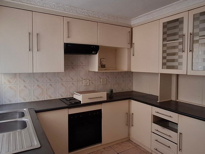 A functional kitchen featuring built-in cabinetry, laminate countertops, a double stainless steel sink, and integrated oven with hob, finished with tiled flooring and backsplash.