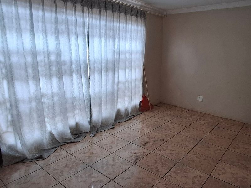 An empty living room featuring tiled flooring and a large sliding glass door with curtains, presenting a blank canvas for potential renovation.