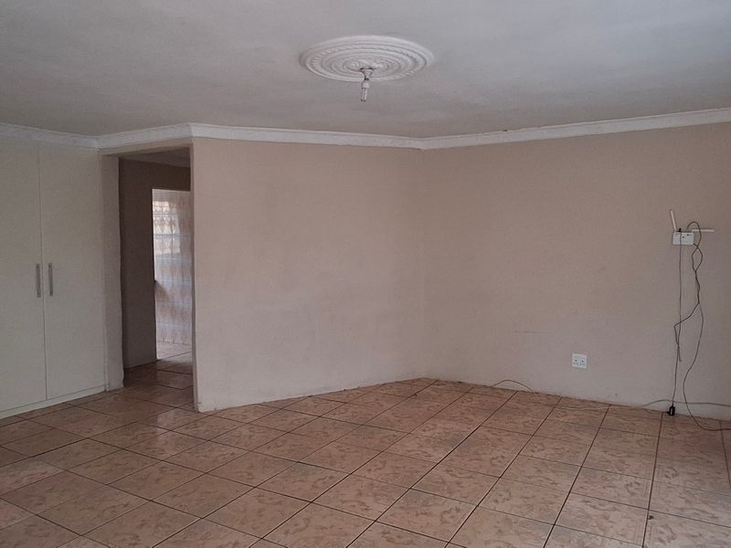 Spacious living area featuring neutral tiled flooring, built-in storage cupboards, and decorative ceiling detailing, offering a blank canvas for interior design.