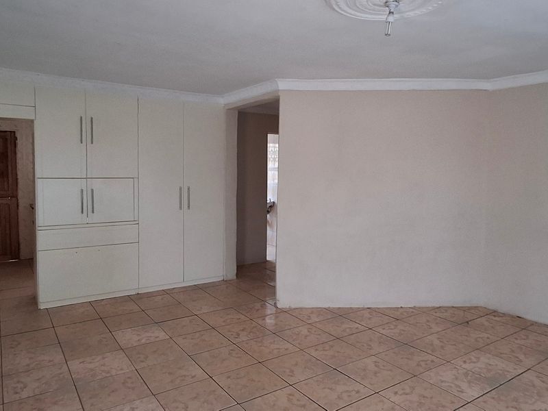 An empty living area featuring ceramic floor tiles, built-in storage cabinetry, and decorative ceiling coving, offering a blank canvas for interior design.
