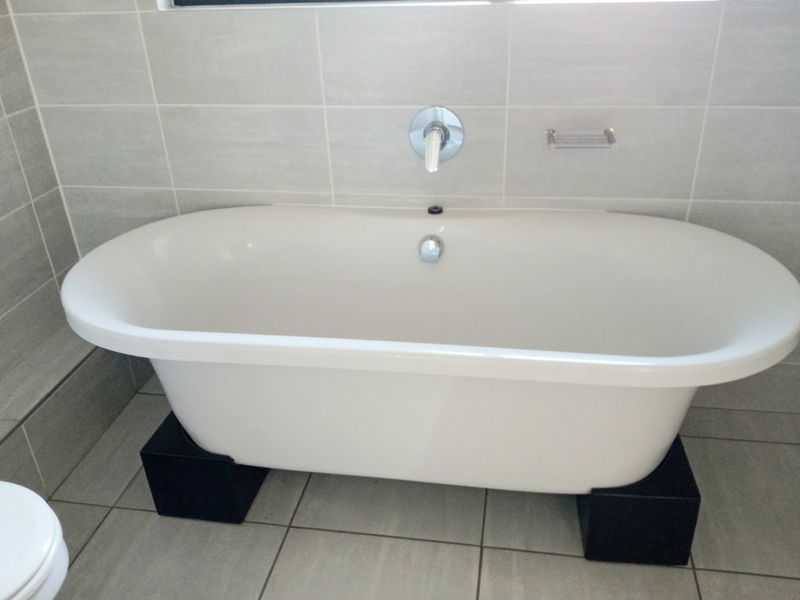 A modern bathroom featuring a white freestanding bathtub with wall-mounted chrome fixtures and neutral ceramic tiling throughout.