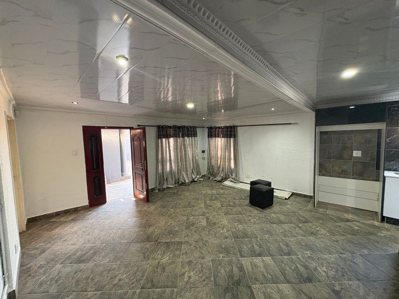 Spacious open-plan living area featuring large floor tiles, recessed ceiling lighting, and decorative molding, with an adjacent kitchen area and direct outdoor access.