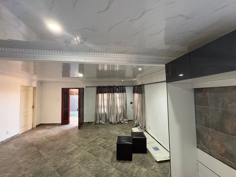 Spacious open-plan living area featuring glossy ceiling panels, tiled flooring, and built-in cabinetry with a tiled splashback, offering a versatile layout.