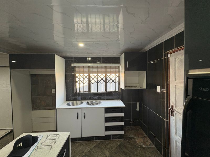 A functional kitchen featuring dark tiled walls, built-in cabinetry, a double sink, and a glossy ceiling finish, offering a blank canvas for updates.