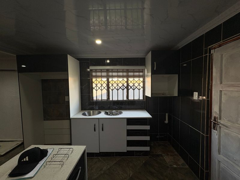 A kitchen area featuring dark wall tiles, built-in cabinetry, and a double bowl sink, currently in an unfinished state requiring completion.