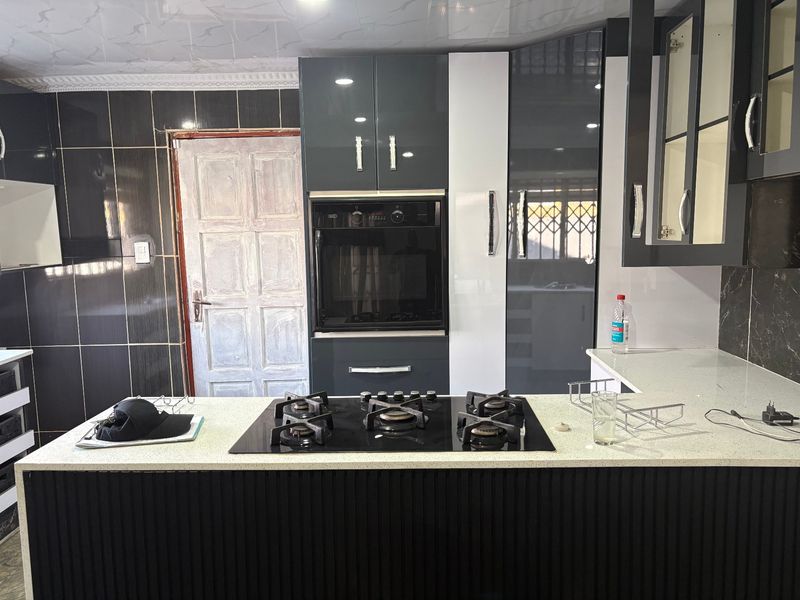 Modern kitchen featuring high-gloss cabinetry, quartz countertops, a built-in oven, and a gas hob, with a contemporary tiled backsplash.