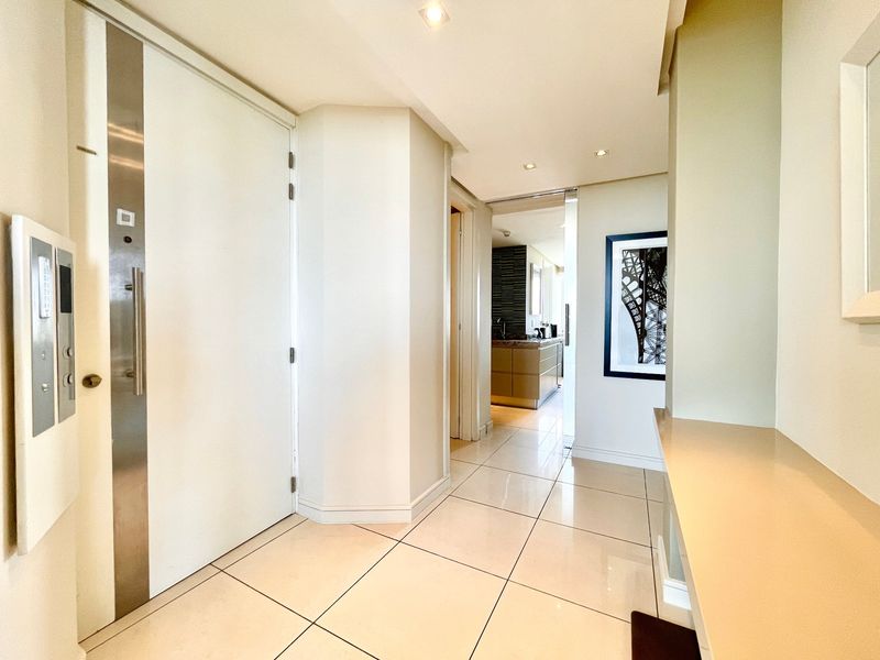 A bright and modern entrance hallway featuring polished tiled flooring, recessed lighting, and a built-in console shelf, leading towards the kitchen area.