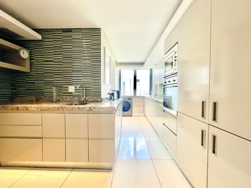 Modern galley-style kitchen featuring sleek cabinetry, stone countertops, integrated appliances, and a striking mosaic tile backsplash with polished floor tiles.