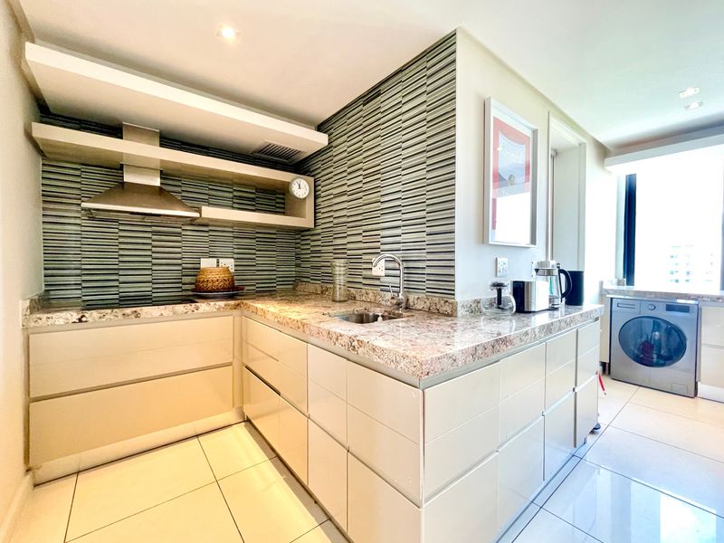 Modern kitchen featuring sleek cabinetry, granite countertops, a tiled backsplash, and integrated stainless steel extractor fan, offering a clean and functional culinary space.