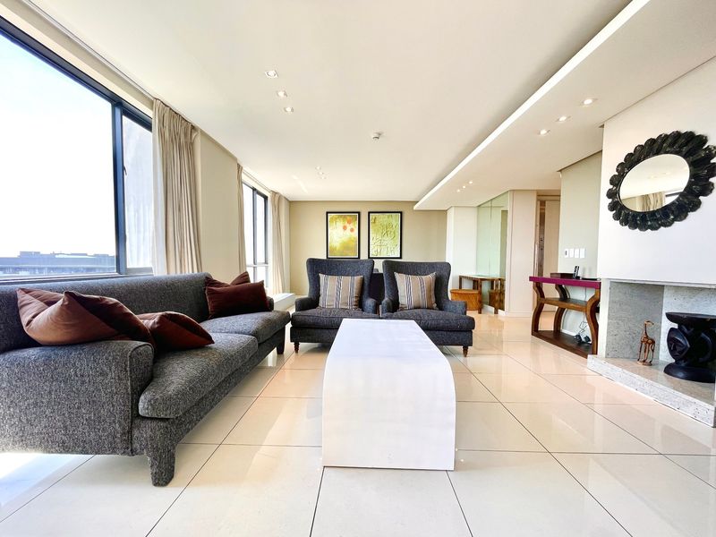 A bright and spacious living room featuring large floor-to-ceiling windows, polished tiled flooring, recessed ceiling lighting, and a modern built-in fireplace.