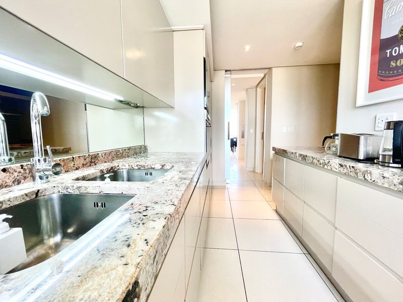Modern galley-style kitchen featuring high-gloss cabinetry, granite countertops, undermount double sink, and sleek tiled flooring with integrated under-cabinet lighting.