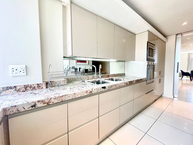 Modern kitchen featuring sleek handleless cabinetry, granite countertops, a mirrored backsplash, and integrated stainless steel appliances, set against clean tiled flooring.