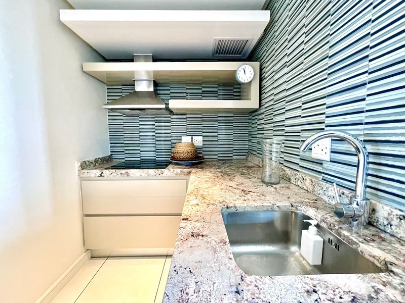 A compact, modern kitchen featuring granite countertops, a stainless steel sink, built-in hob with extractor fan, and decorative tiled backsplash.
