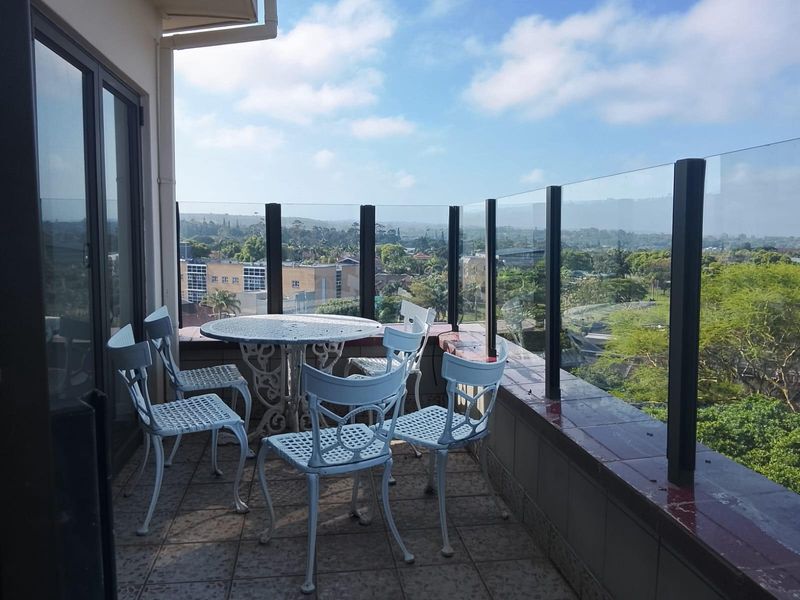 A spacious balcony featuring a glass balustrade and tiled flooring, offering expansive views of the surrounding neighborhood and landscape.