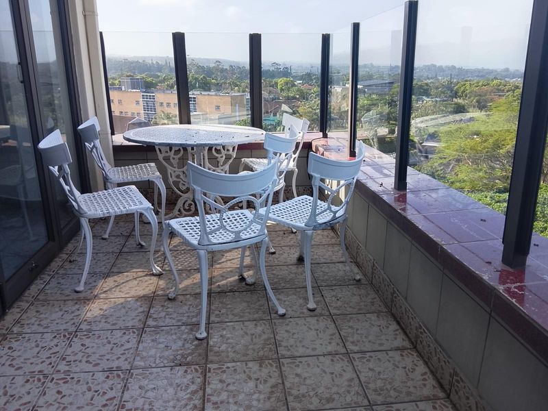 A balcony featuring a glass balustrade and tiled flooring, offering elevated views of the surrounding neighborhood.