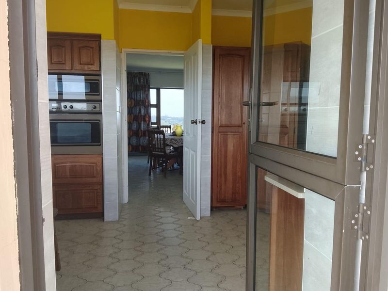 A dated kitchen area featuring built-in wooden cabinetry, integrated oven and microwave, and tiled flooring, with a view through to the adjacent living space.