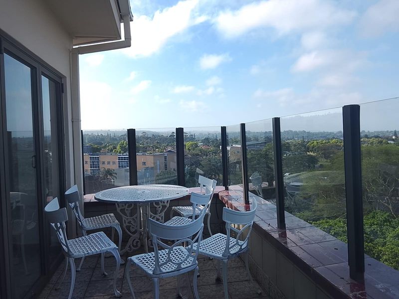 A spacious balcony featuring a glass balustrade and tiled flooring, offering expansive elevated views of the surrounding neighborhood.