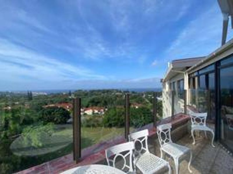 Spacious balcony featuring a glass balustrade and tiled flooring, offering expansive elevated views of the surrounding landscape and coastline.