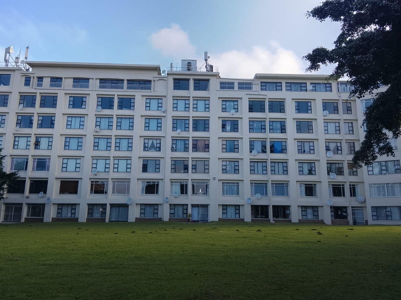A view of the rear facade of a multi-story apartment building featuring numerous windows, balconies, and an expansive communal lawn area.