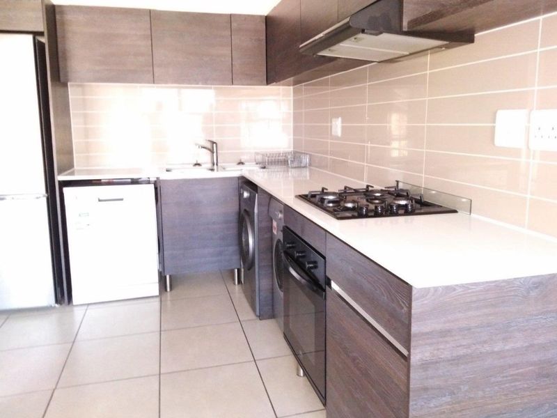 Modern kitchen featuring dark wood-grain cabinetry, stone countertops, gas hob, extractor fan, and tiled splashback with integrated appliance spaces.