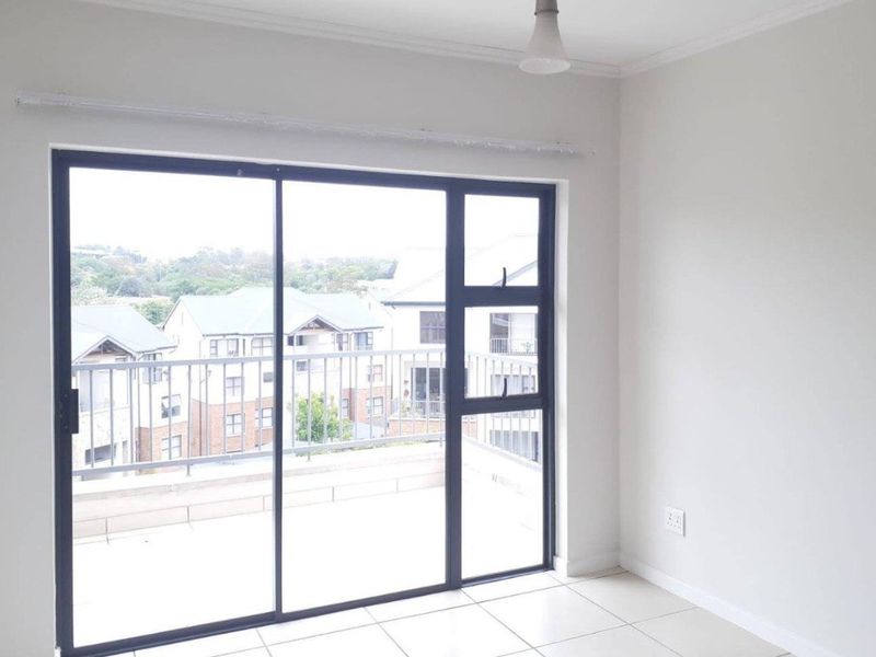 A bright, empty living area featuring neutral tiled flooring and large sliding glass doors that provide direct access to an outdoor balcony.