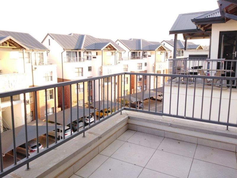 A spacious balcony featuring tiled flooring and a metal balustrade, offering an elevated view of the apartment complex and covered parking area.