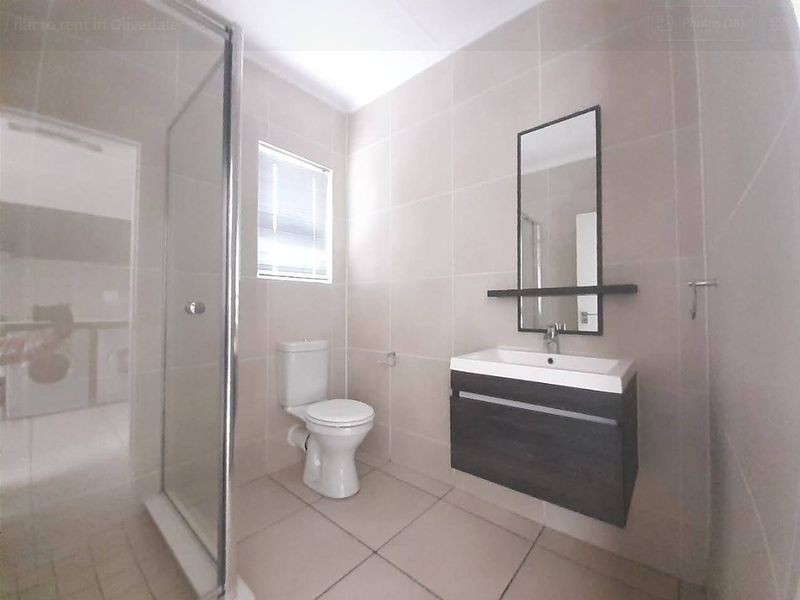 A clean, modern bathroom featuring a glass shower enclosure, a wall-mounted vanity with a basin, and neutral floor-to-ceiling tiling.