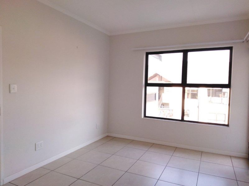 A clean, empty bedroom featuring neutral tiled flooring, white walls, and a large aluminium-framed window providing natural light.