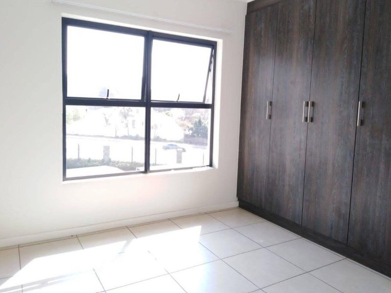 A bright, empty bedroom featuring modern dark wood built-in cupboards, neutral tiled flooring, and a large aluminium-framed window.