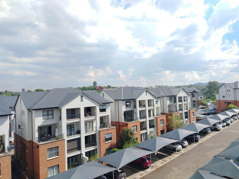 An elevated aerial view of a modern apartment complex featuring brick and plaster facades, pitched roofs, private balconies, and covered parking bays.