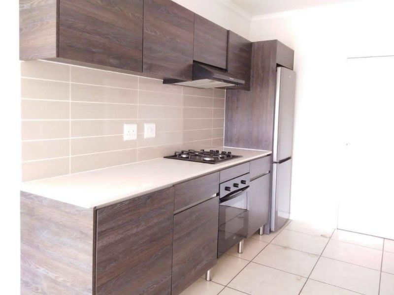 Modern kitchen featuring dark wood-look cabinetry, a gas hob, built-in oven, extractor fan, and neutral tiled backsplash.