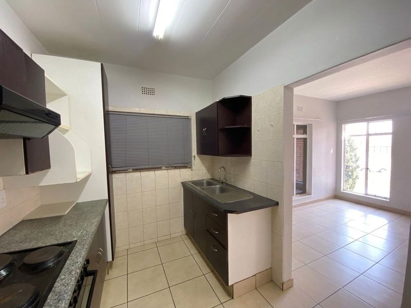 A functional kitchen featuring built-in cabinetry, a double sink, tiled splashbacks, and a ceramic hob, adjacent to an open-plan living area.