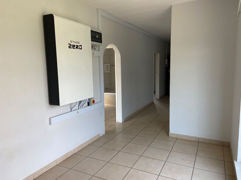 A spacious hallway featuring tiled flooring, an arched doorway, and a wall-mounted solar battery storage system.